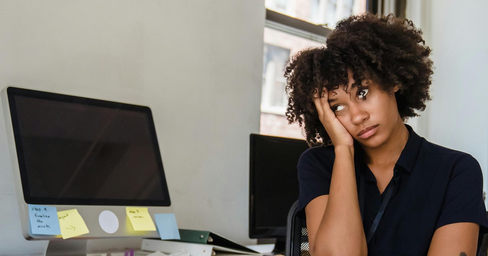 Employee sat with her head in her hand, bored at an office desk. 